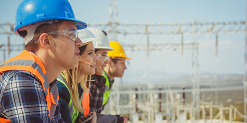 Drei Ingenieure schauen in die Ferne vor einer Baustelle.
